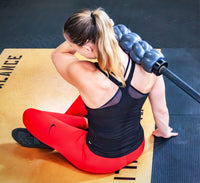 Athlete using a foam roller that fits on a barbell to massage the upper trapezius muscles